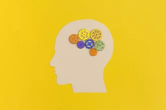 Sagoma di una testa con ingranaggi colorati al suo interno su sfondo giallo.