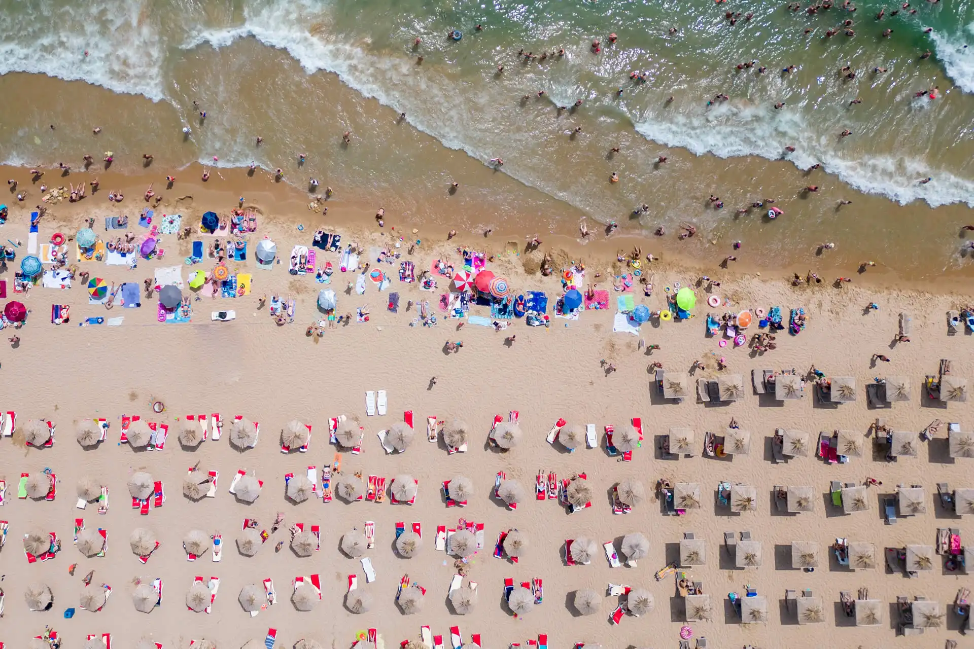 Vista dall'alto di una spiaggia affollata con ombrelloni e bagnanti.