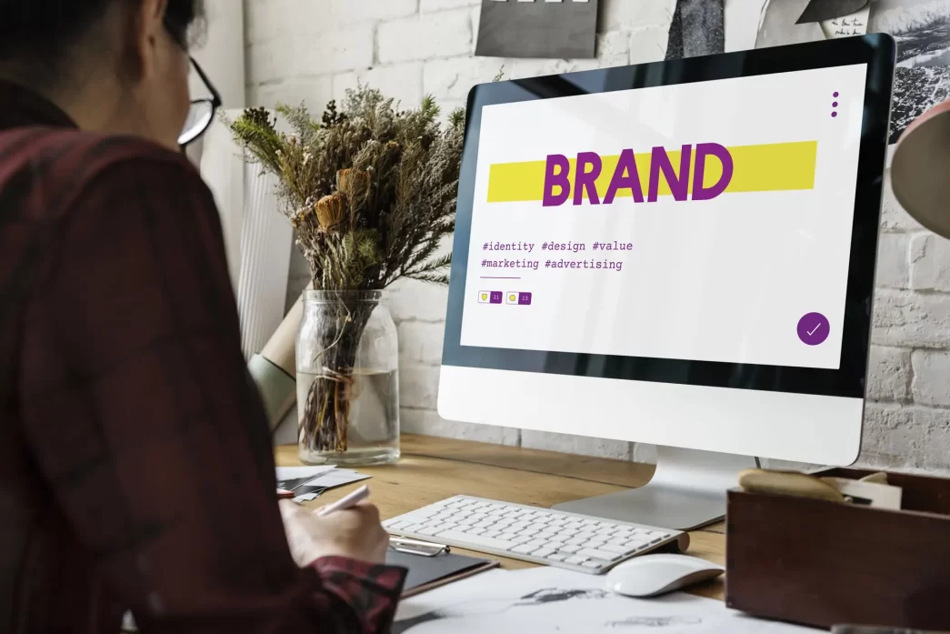 Persona che lavora al computer con schermata che mostra il branding e parole chiave come identità, design, valore e marketing.