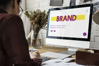 Persona che lavora al computer con schermata che mostra il branding e parole chiave come identità, design, valore e marketing.