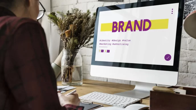 Persona che lavora al computer con schermata che mostra il branding e parole chiave come identità, design, valore e marketing.