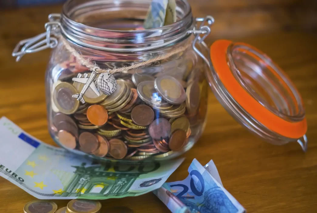 Salvadanaio di vetro pieno di monete con banconote euro sul tavolo.