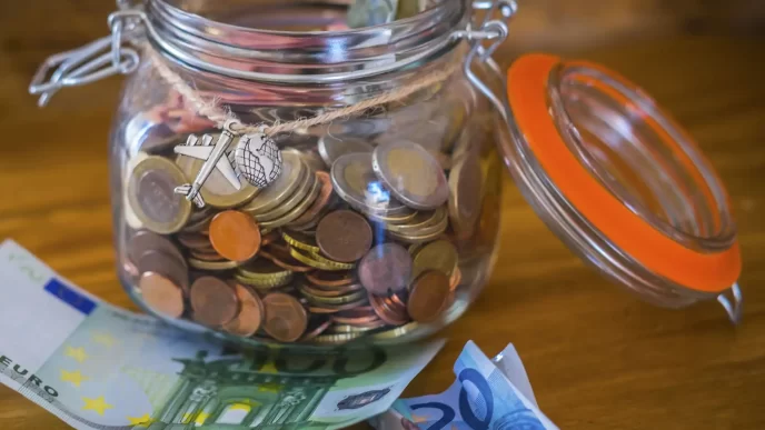 Salvadanaio di vetro pieno di monete con banconote euro sul tavolo.
