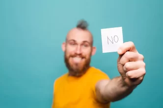 Uomo sorridente con barba che mostra un cartello con la scritta 'NO'.