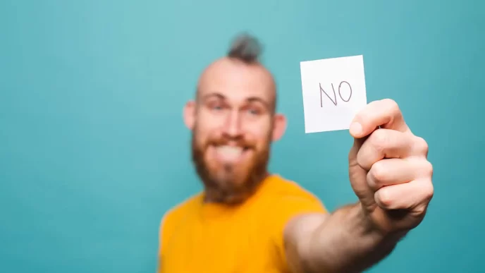 Uomo sorridente con barba che mostra un cartello con la scritta 'NO'.