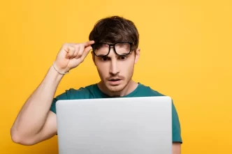 Uomo sorpreso guarda il computer con sfondo giallo.