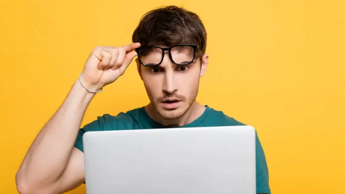 Uomo sorpreso guarda il computer con sfondo giallo.
