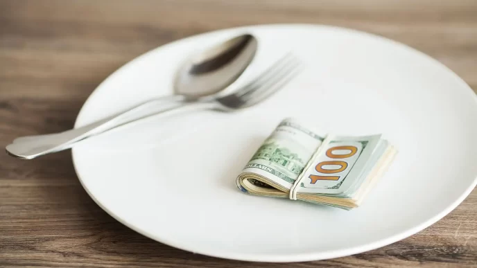 Banconote da 100 dollari arrotolate su un piatto bianco con posate.