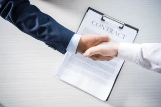 Stretta di mano tra due persone sopra un contratto, simbolo di accordo commerciale o prenotazione alberghiera.