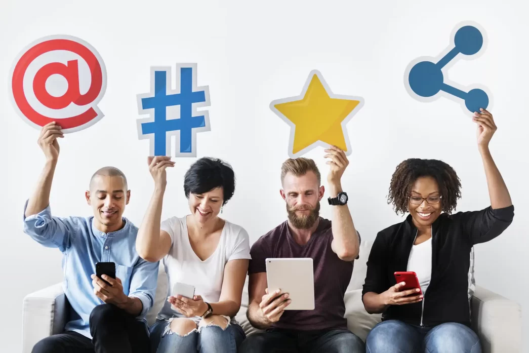 Persone che tengono simboli di social media come chiocciola, hashtag, stella e condivisione.