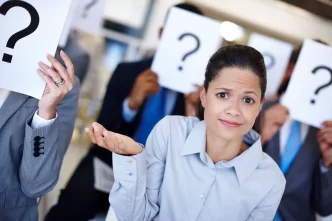 Donna perplessa davanti a persone che tengono cartelli con punti interrogativi, concetto di incertezza.