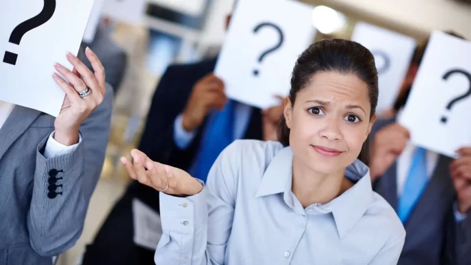 Donna perplessa davanti a persone che tengono cartelli con punti interrogativi, concetto di incertezza.