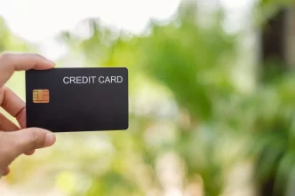 Primo piano di una mano che tiene una carta di credito nera con uno sfondo verde sfocato.