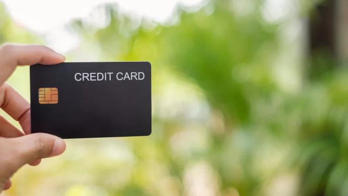 Primo piano di una mano che tiene una carta di credito nera con uno sfondo verde sfocato.