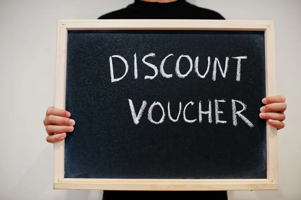 Persona che tiene una lavagna con la scritta 'Discount Voucher', su sfondo neutro.