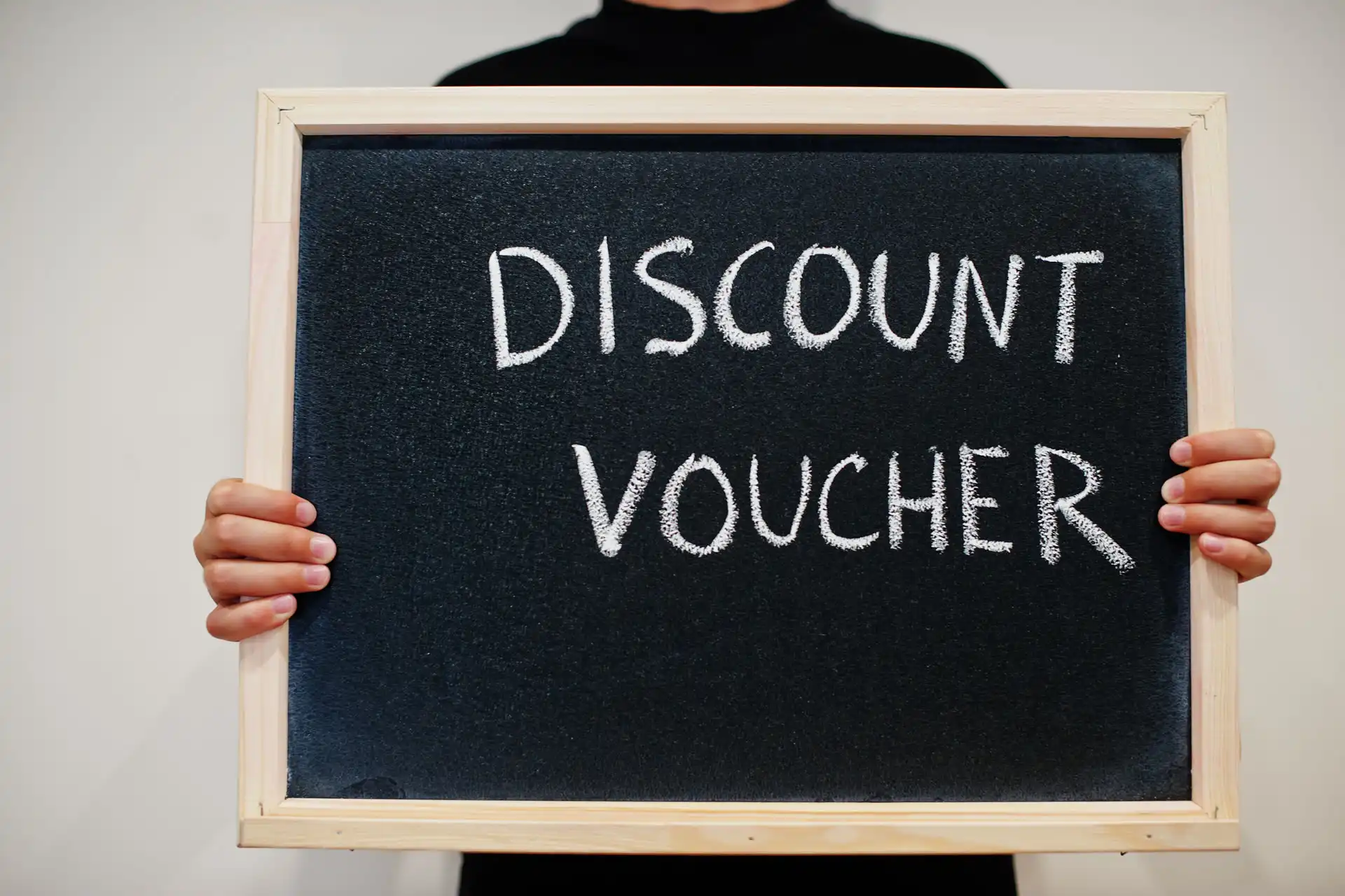 Persona che tiene una lavagna con la scritta 'Discount Voucher', su sfondo neutro.