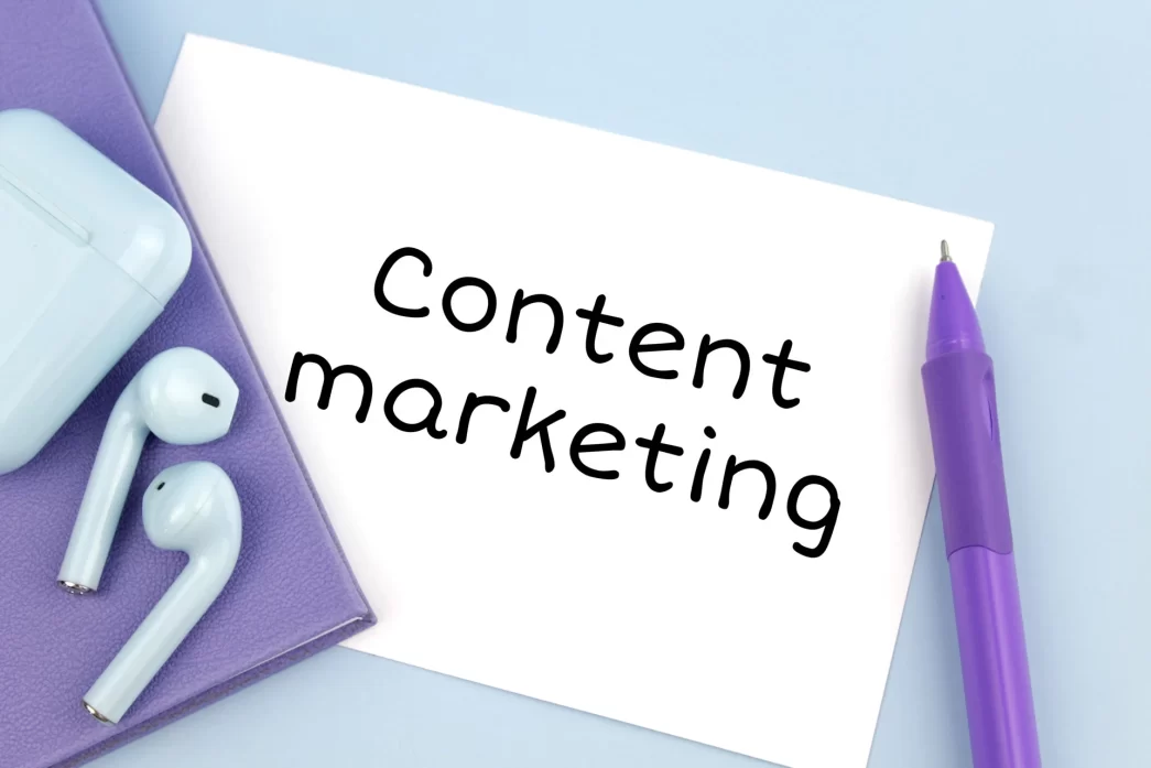 AirPods bianchi e penna viola su quaderno viola con nota 'Content marketing'