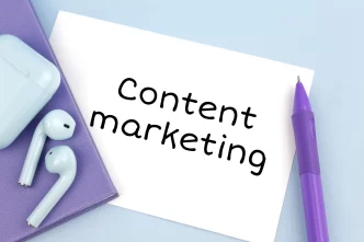 AirPods bianchi e penna viola su quaderno viola con nota 'Content marketing'