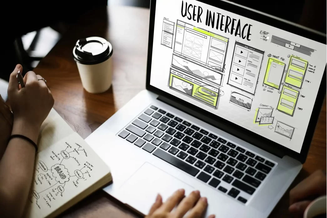 Schermata di progettazione dell'interfaccia utente su laptop con appunti su brand e tazza di caffè sul tavolo.