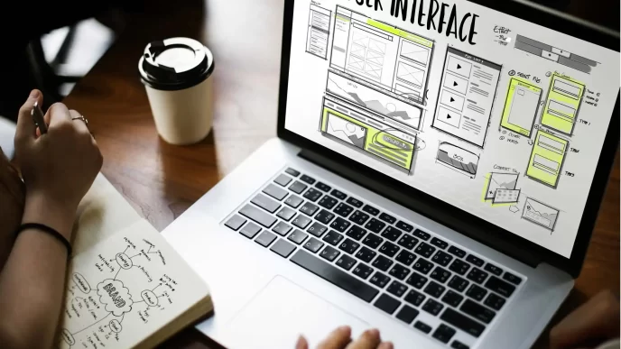 Schermata di progettazione dell'interfaccia utente su laptop con appunti su brand e tazza di caffè sul tavolo.