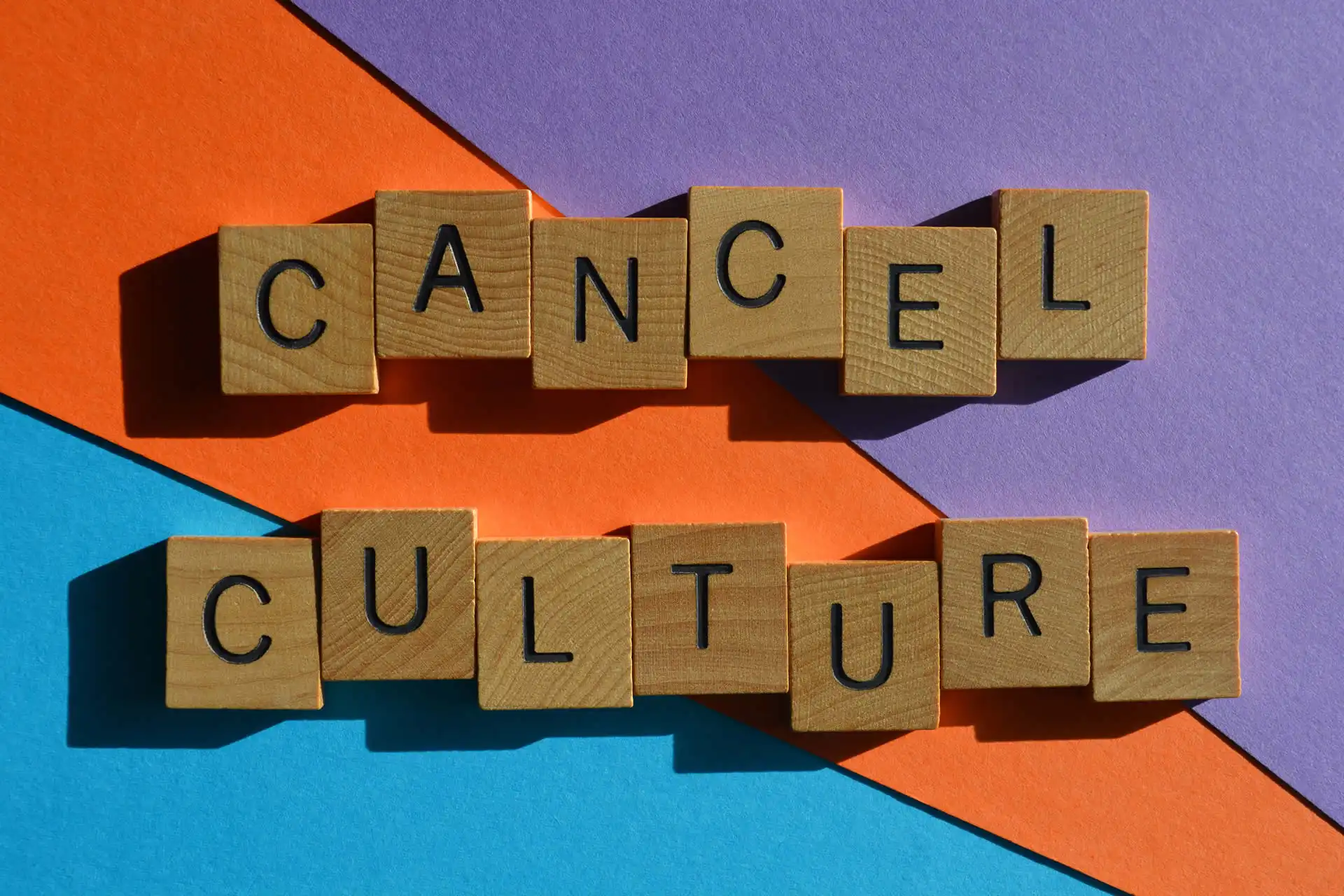 Immagine con scritta 'Cancel Culture' composta da lettere di legno su sfondo colorato arancione, blu e viola.