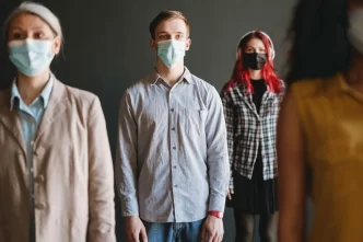 Persone che indossano mascherine facciali protettive in piedi mantenendo il distanziamento sociale.