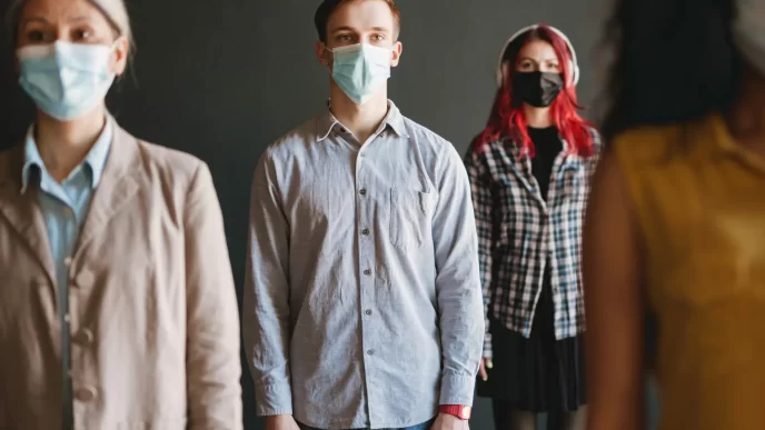 Persone che indossano mascherine facciali protettive in piedi mantenendo il distanziamento sociale.