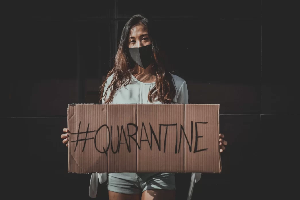 Donna con mascherina che tiene un cartello con la scritta #QUARANTINE durante la pandemia di COVID-19.