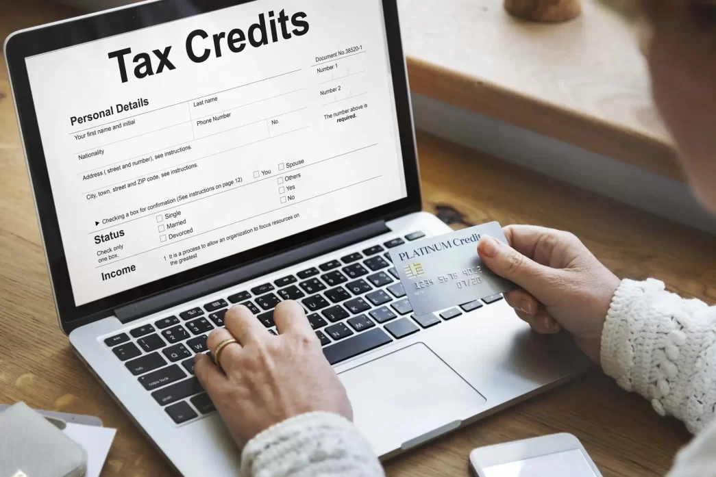 Riqualificazione Alberghi: Persona che utilizza un computer portatile per compilare un modulo di richiesta crediti d'imposta, tenendo una carta di credito.