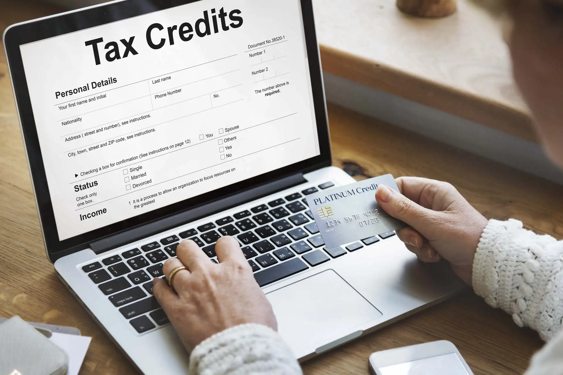 Riqualificazione Alberghi: Persona che utilizza un computer portatile per compilare un modulo di richiesta crediti d'imposta, tenendo una carta di credito.