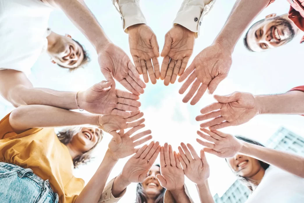Gruppo di giovani all'aperto che si uniscono mettendo le mani insieme in cerchio, simbolo di unità e lavoro di squadra.
