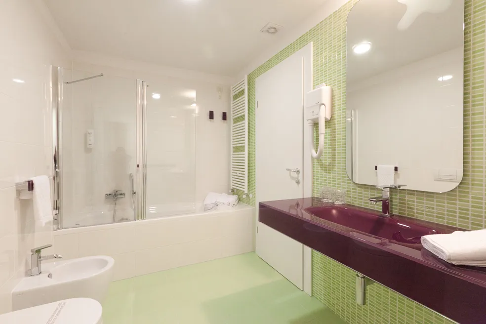 Bagno dell'hotel con arredi moderni, piastrelle verdi e lavabo viola.