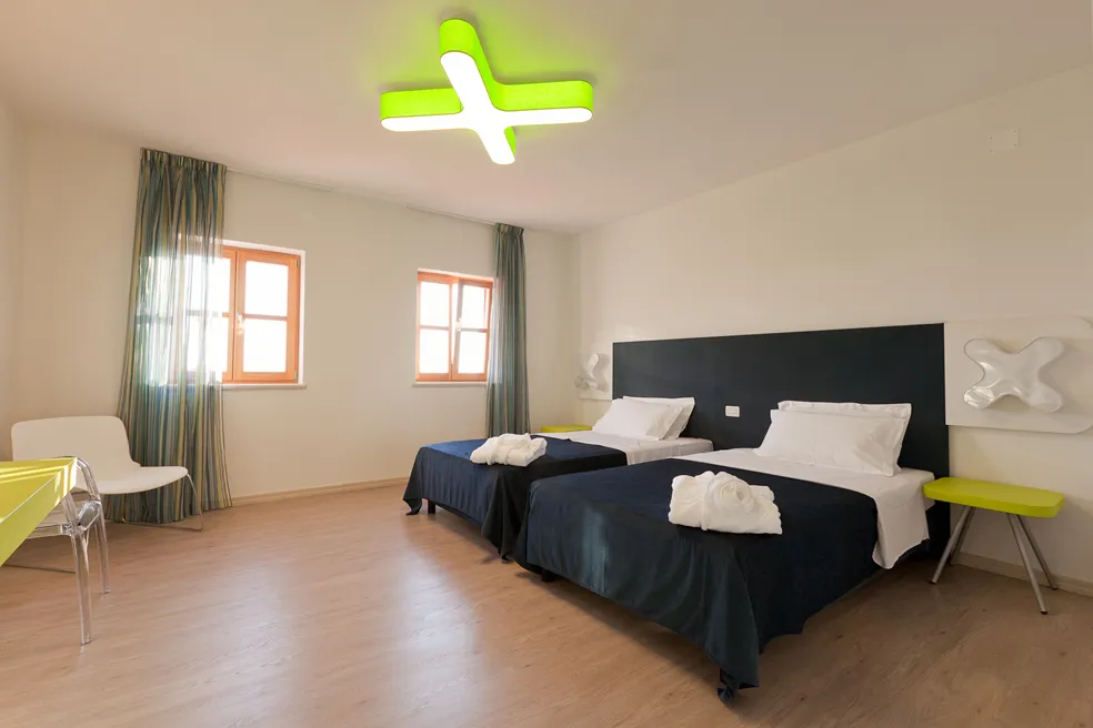 Camera d'hotel con letti gemelli, accenti verdi e luce naturale dalle finestre.