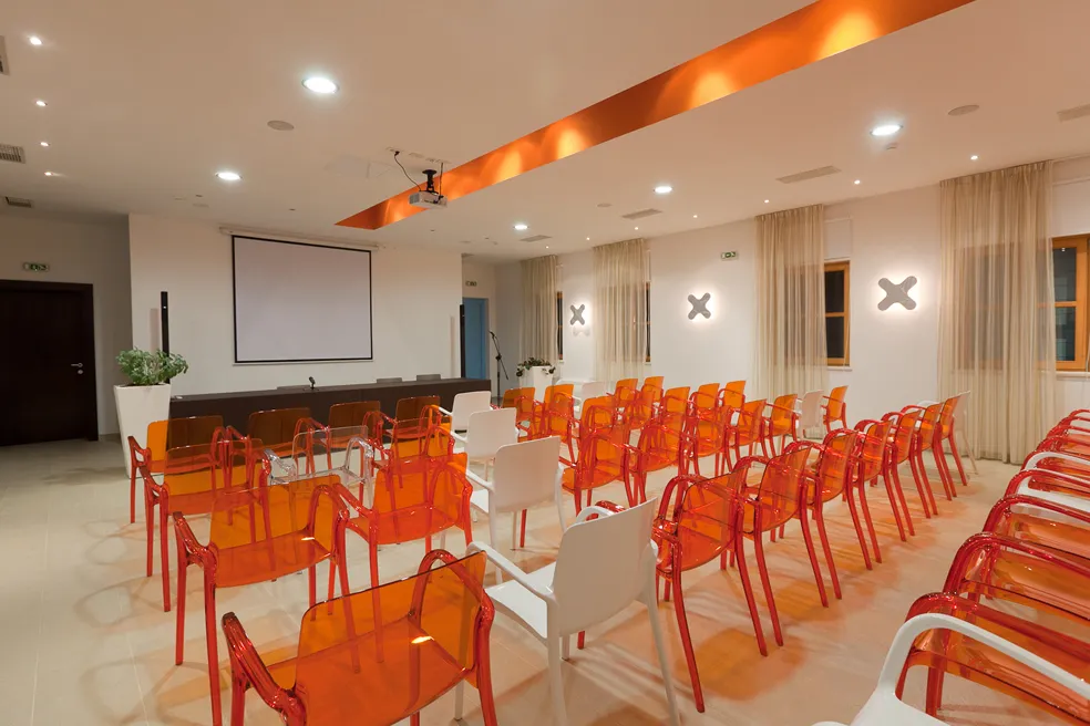 Sala conferenze con sedie arancioni e bianche, proiettore e schermo.