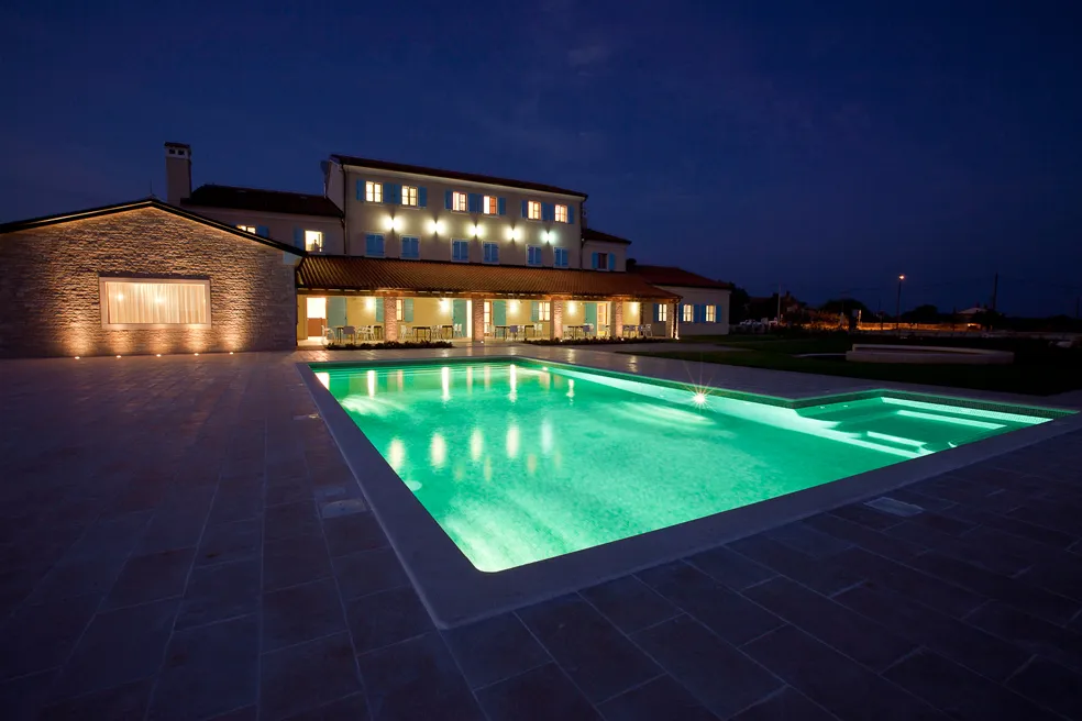 Vista notturna dell'hotel con piscina illuminata e luci esterne.