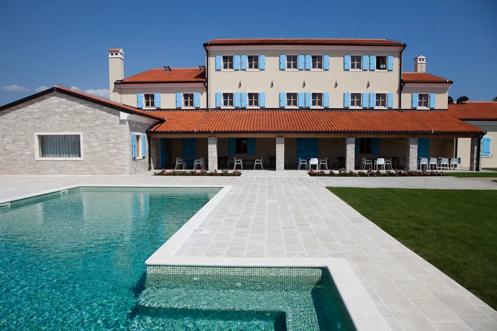 Vista diurna dell'hotel con cielo sereno, piscina esterna e prato verde.