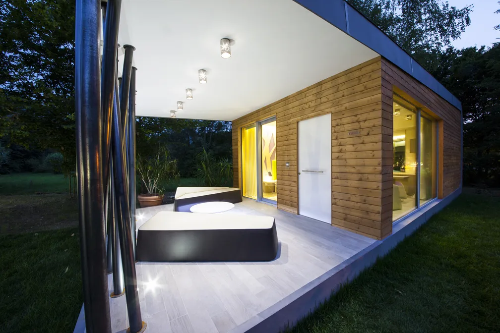 Patio esterno illuminato di sera di una casa moderna con elementi in legno.