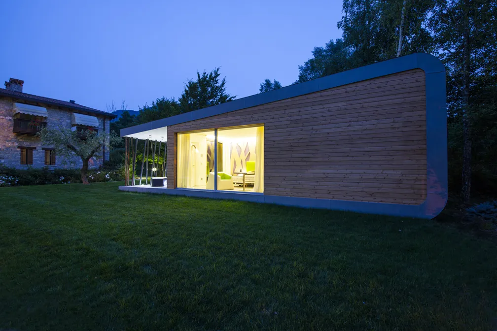 Casa moderna illuminata di notte con ampie vetrate e giardino verde.