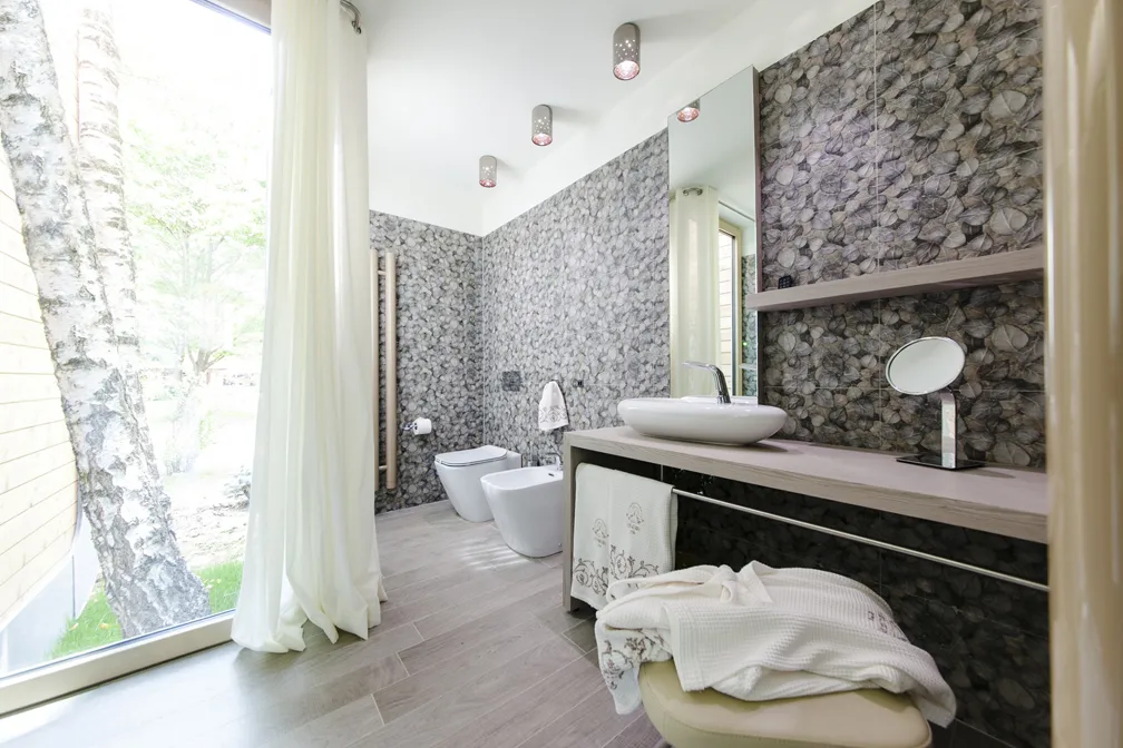 Bagno moderno con ampie finestre, lavabo e bidet, decorato con pietre.