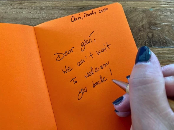 Messaggio scritto a mano su un foglio arancione che esprime il desiderio di accogliere di nuovo gli ospiti all'Oasi.