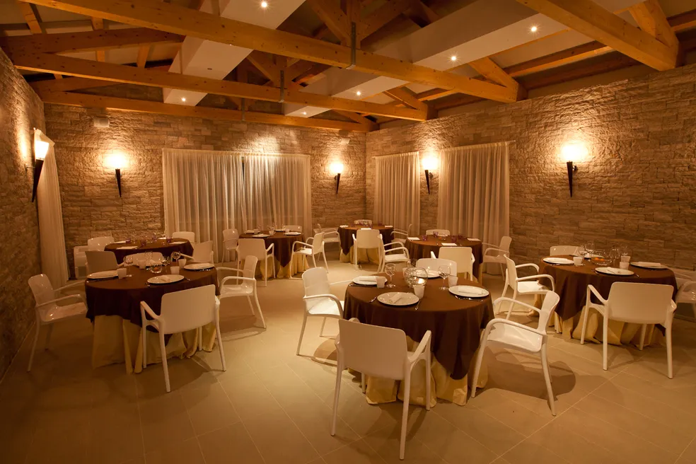 Ristorante elegante con pareti in pietra, travi in legno al soffitto e tavoli rotondi.