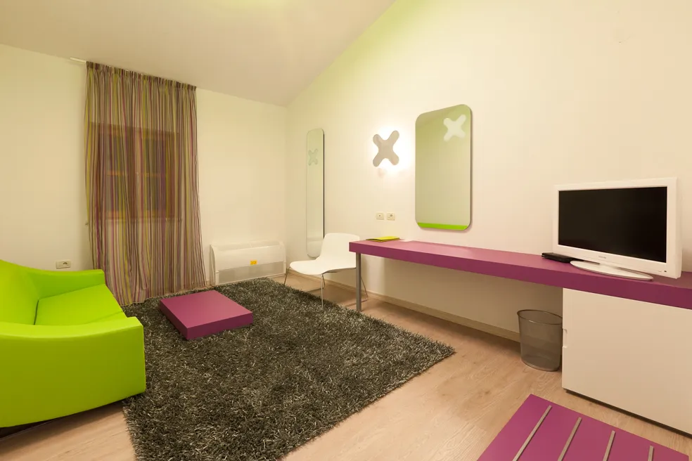  Suite dell'hotel con arredamento vivace verde e viola, TV e ambiente accogliente.