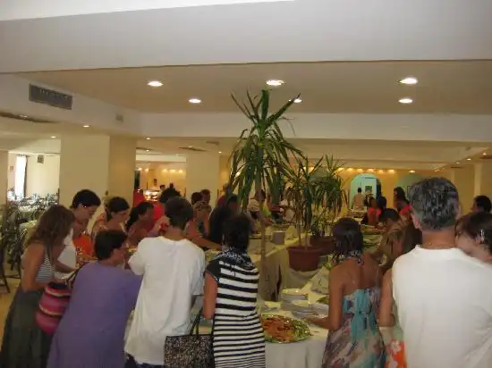 Persone affollate intorno a un buffet in un ambiente interno illuminato.
