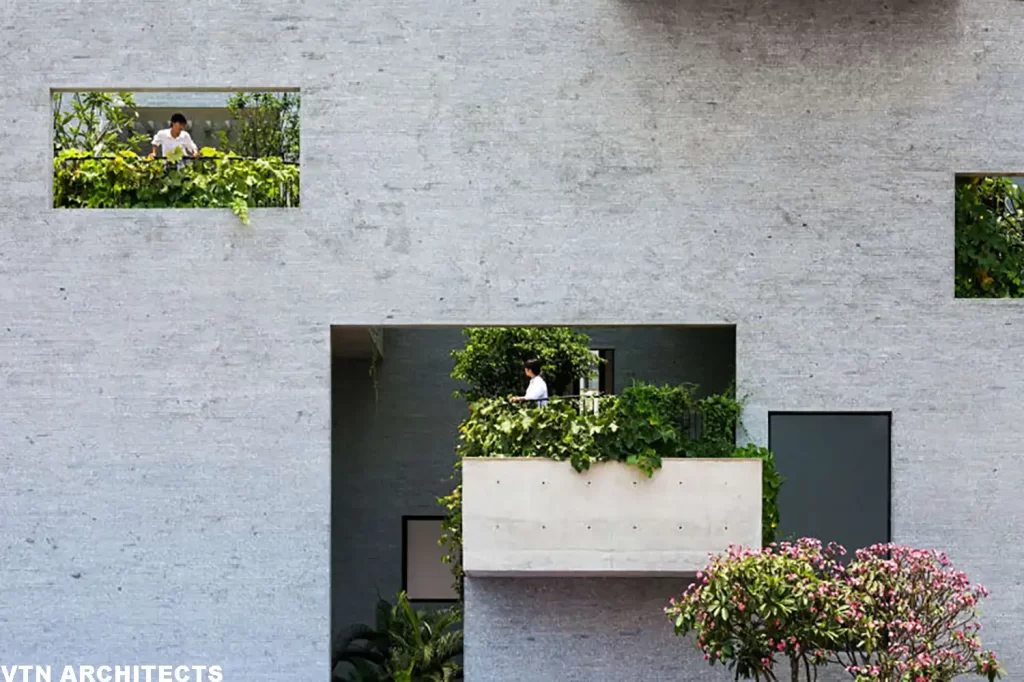 Facciata di edificio moderno con giardini verticali integrati e una persona in piedi sul balcone.