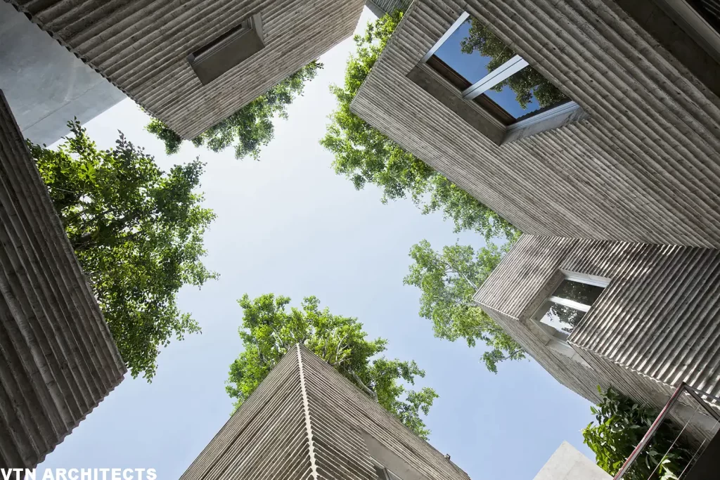 Vista dal basso di edifici moderni con cortile verde e alberi che crescono tra le strutture.

