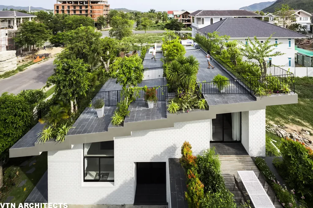 Edificio moderno con terrazza verde e piante, vista dall'alto con una persona che cammina sulla terrazza.
