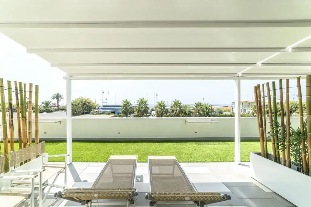 Terrazza di un hotel con sedie a sdraio, prato e vista sul mare, arredata con elementi in bambù.
