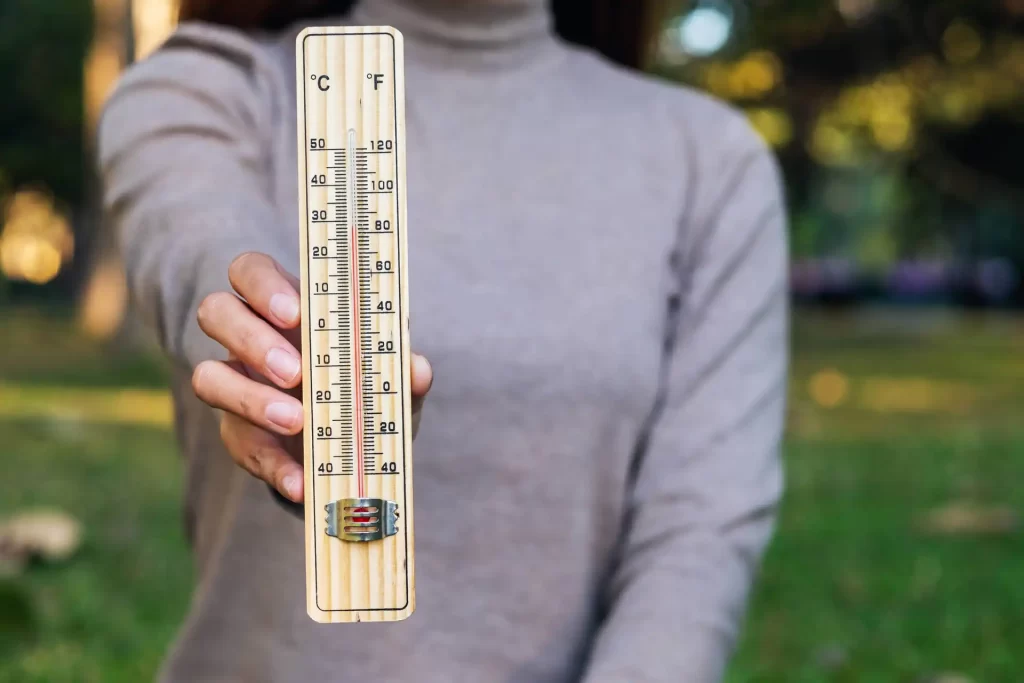 Primo piano di una donna che tiene in mano un termometro di legno che mostra la temperatura in °C e °F.